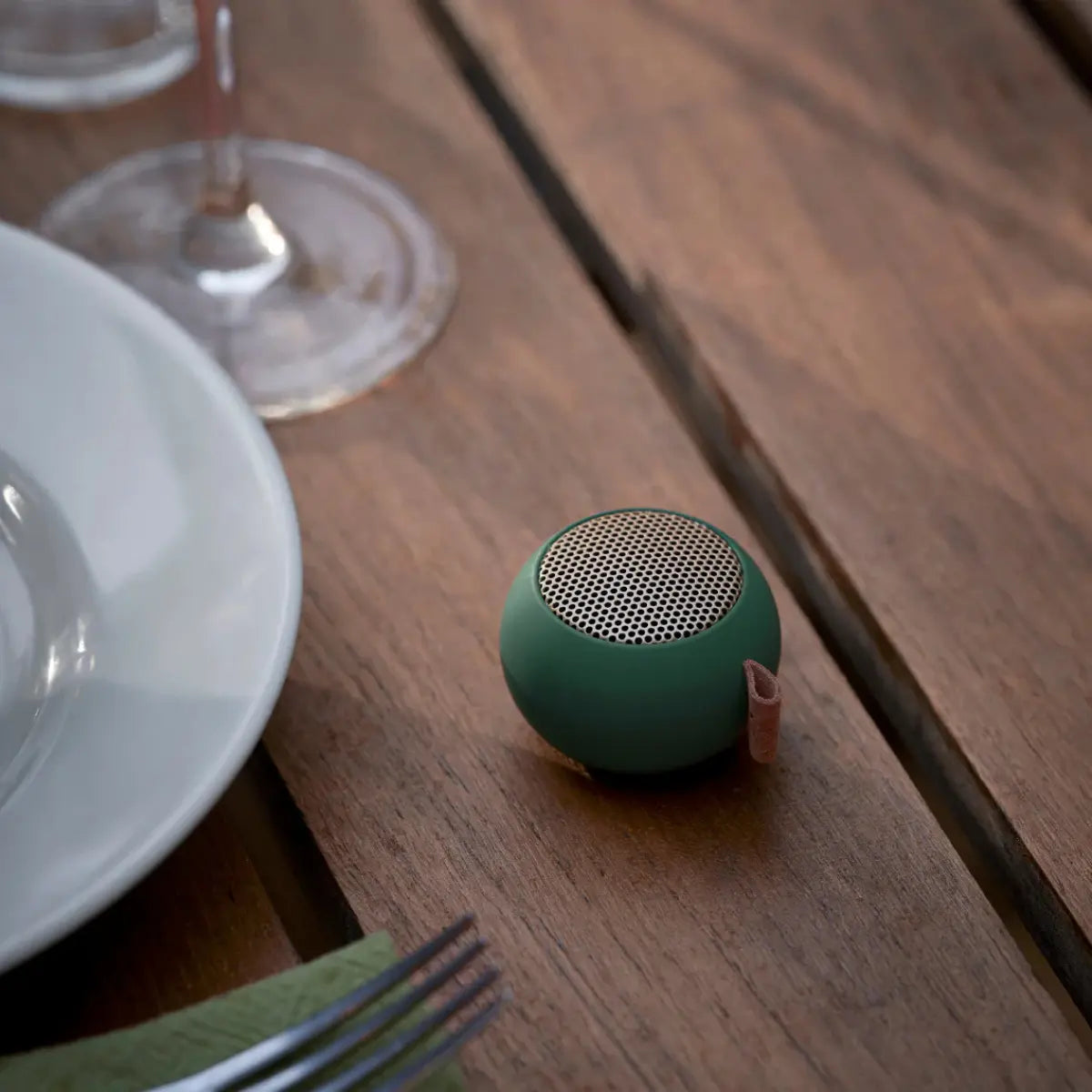 una mini casse audio portatili verde scuro, su tavolo legno. 